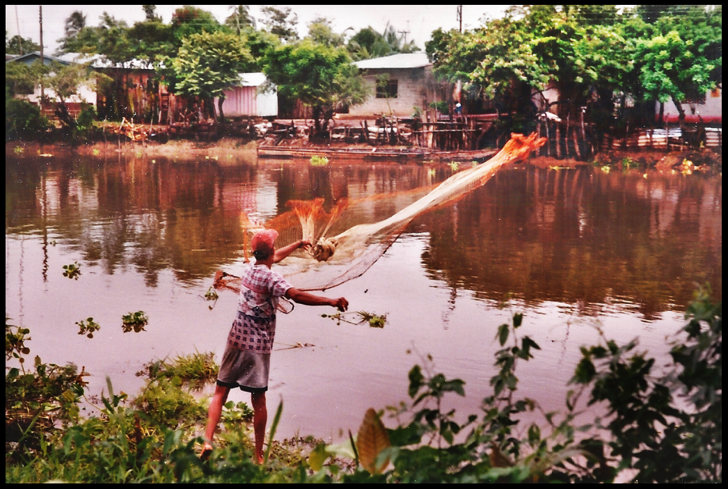 Pedro expertly tossing net
              into Rio Mojana, houses on bank