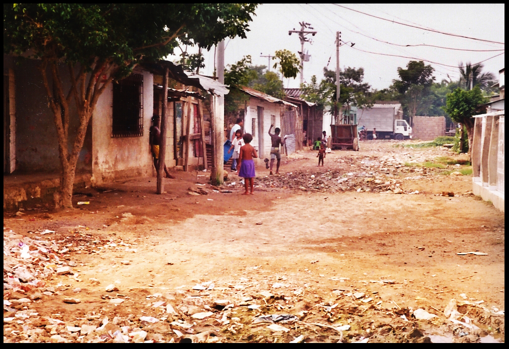 several
              cinderblock huts along a Pozón littered street with
              barely clad children playing