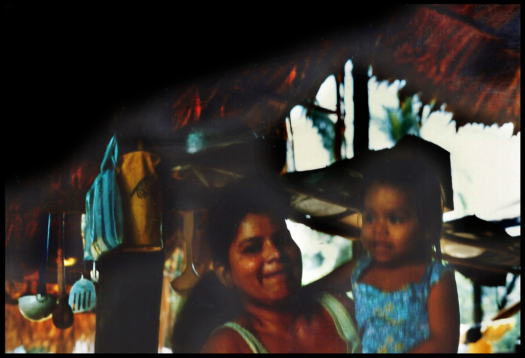 Rosana and 3 year-old
              daughter with cooking utensils hanging from the
              thatch-roof rafters