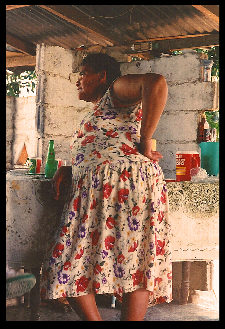 hand on hip, Victoria contemplates
              in her cinderblock open-air kitchen