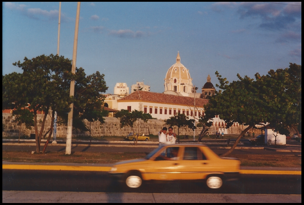 blurred diminutive moving
              yellow cab with park and ancient domed Spanish baroque
              church