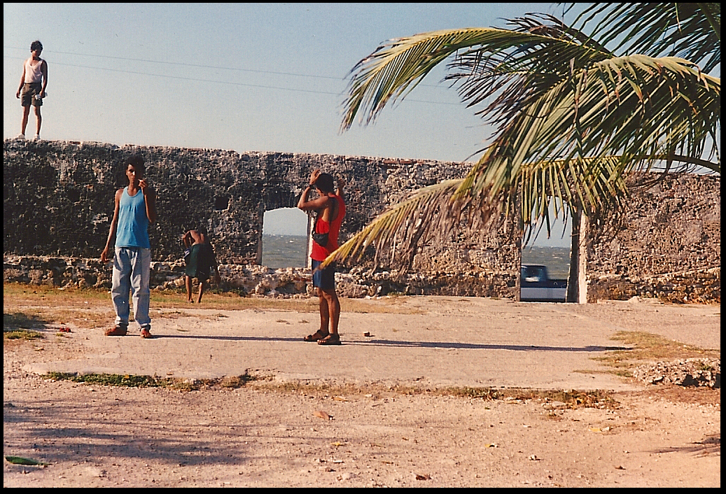 late teen boys in sandy area
              inside ancient city wall, through whose portals the
              Caribbean is seen