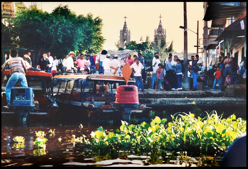 throngs crowd the main docks in
            Santisima Cruz; plaza on market day, church's 2 towers