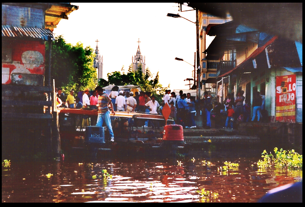 twin church towers and brightly painted plaza shops
            welcome river launch passengers in early morning light