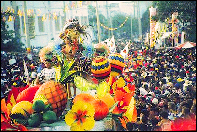 2 floats with huge fruits and
              flowers mobbed by festive humanity in a Barranquilla
              street