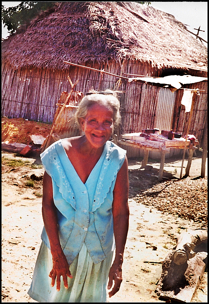 smiling toothless elderly S.
              Cruz lady in dirty housedress in front of her thatched
              stick-and-daub home