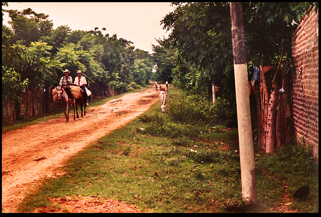 2 men ride loaded horses into
              Santisima Cruz from the countryside