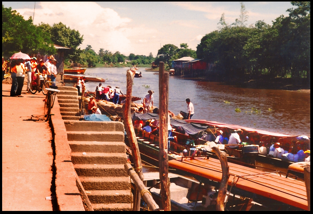 men in straw hats, women with
              parasols, in and beside many motor launches at river
              docks