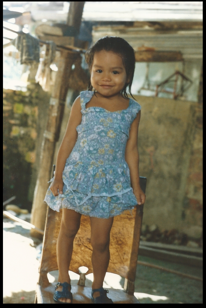 three year old with sweet
              smile stands on chair holding her pretty flowered skirt