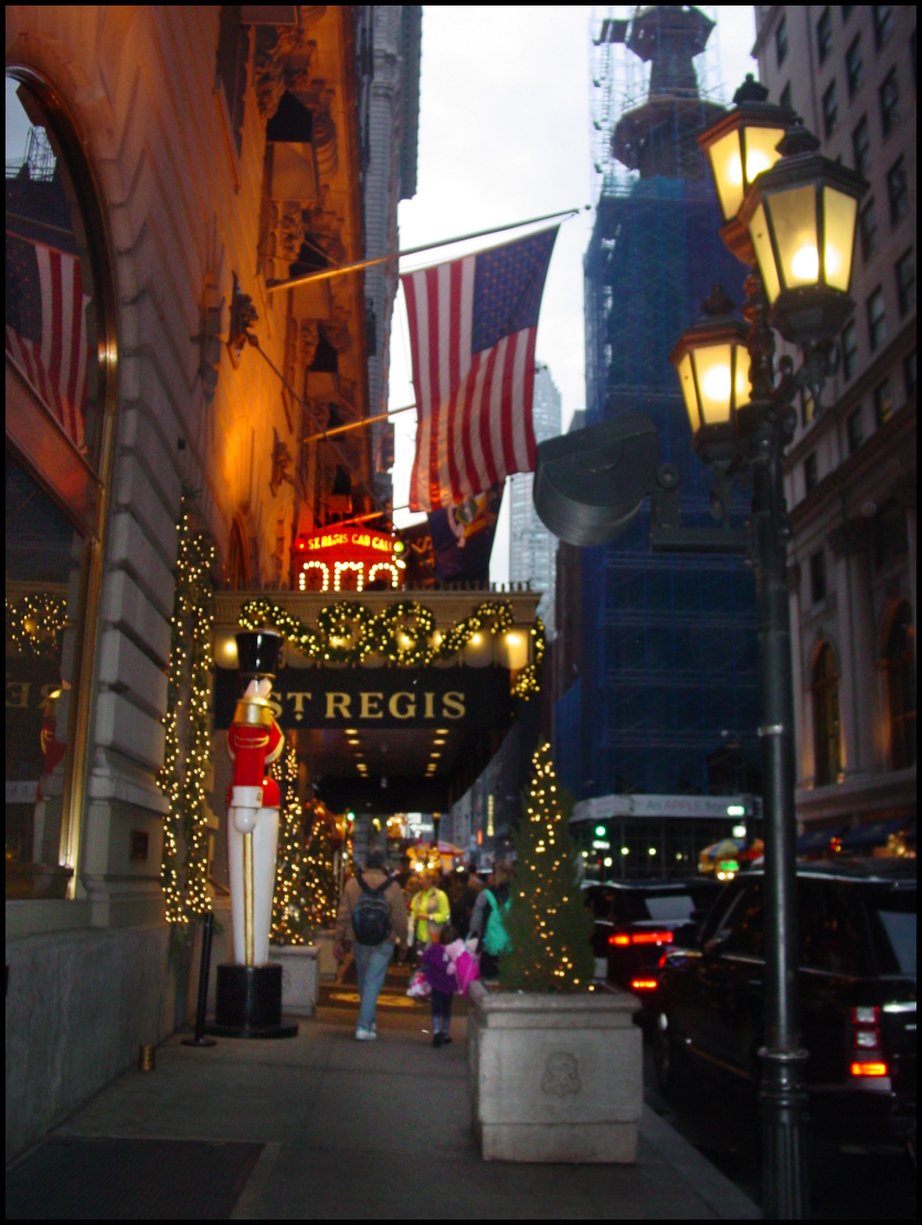 entrance to classy 5th
            Ave. hotel at dusk, with giant nutcracker, Xmas trees and
            people with luggage