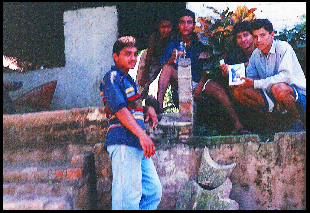 4 twenty-ish boys and one
              tagalong pose stooping and gangle-legged on a porch