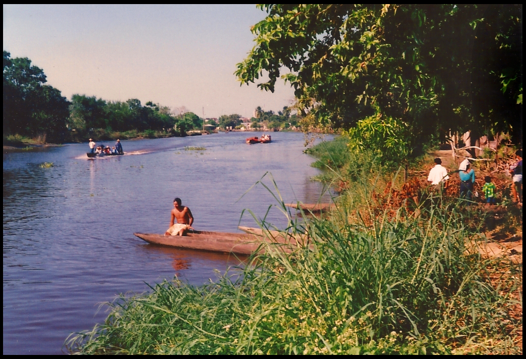 shirtless teen rests on prow
              of dugout in river, surrounded by passengers ferries, lush
              trees and picnickers