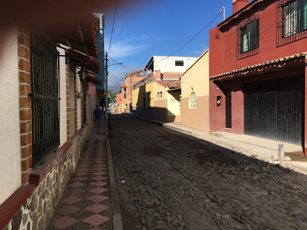 narrow
              cobblestoned street narrows to infinity in the far
              distance, shadowed by earth-tone homes under a deep blue
              sky