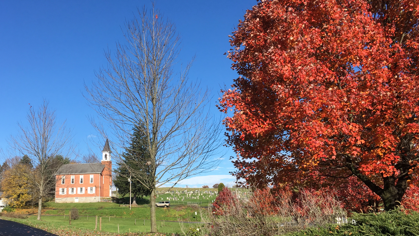 left to right: tall
              brick old country church, cemetery on a hill, red fall
              foliage on a tree