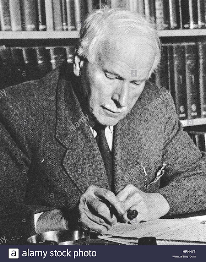 elderly, white-haired Jung in wool tweed
              jacket with pipe at his desk before shelves laden with
              books, black and white photo