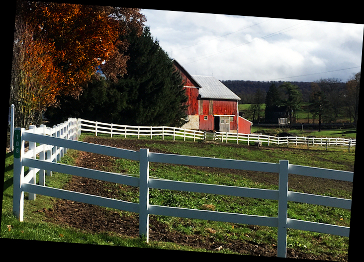 typical neat and tidy
              Pennsylvania red barn with white fences and cloudy sky and
              fall colors in trees